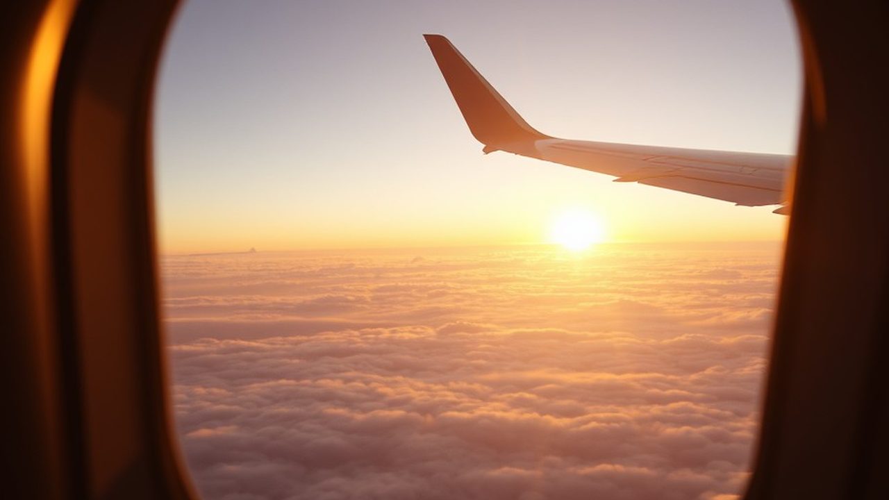 Aircraft wing above the clouds at sunrise seen through a cabin window, illustrating the streamlined non-residency requirement and its 330-day test